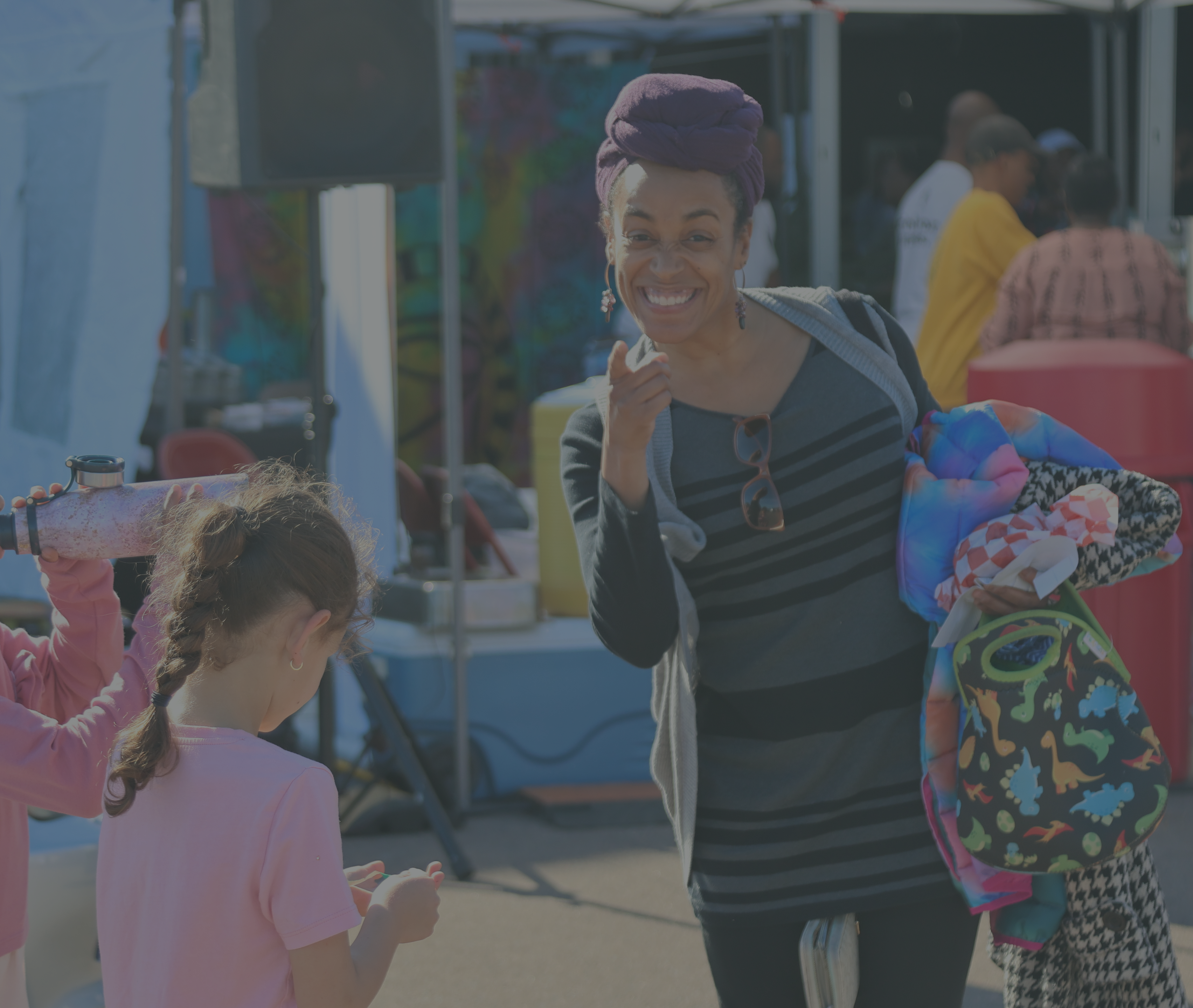An outdoor event, probably a festival, with a group of people and colorful background. [Caption: Outdoor event, probably a...