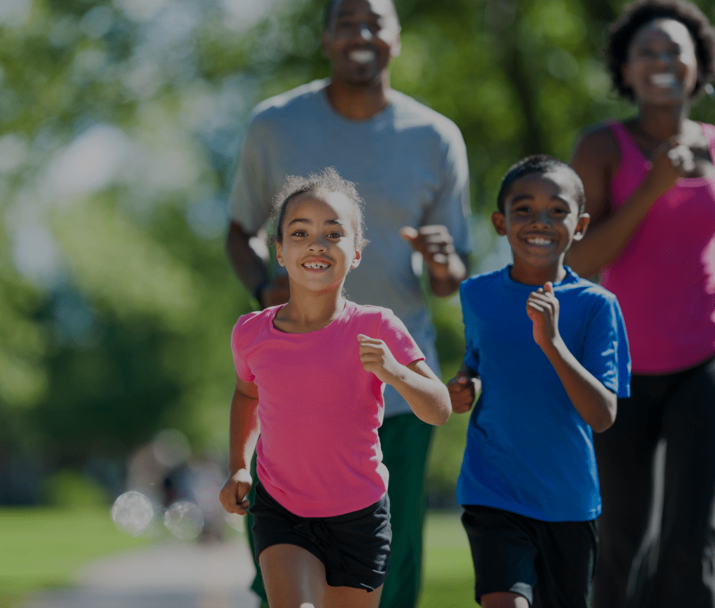 A family of four runs together in a park, captured in a blurry photo due to the weather. The family consists of a young gi...